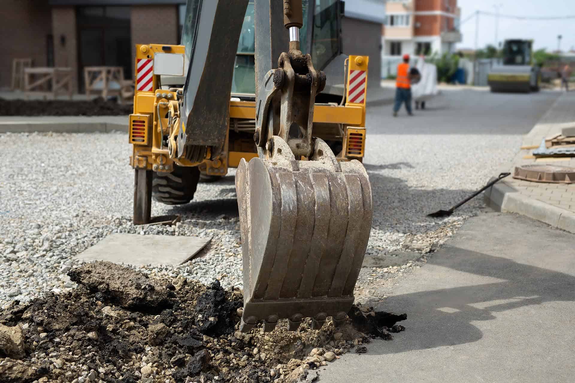 Bucket of the excavator breaks the old asphalt. Work on the dismantling and repair of the road.